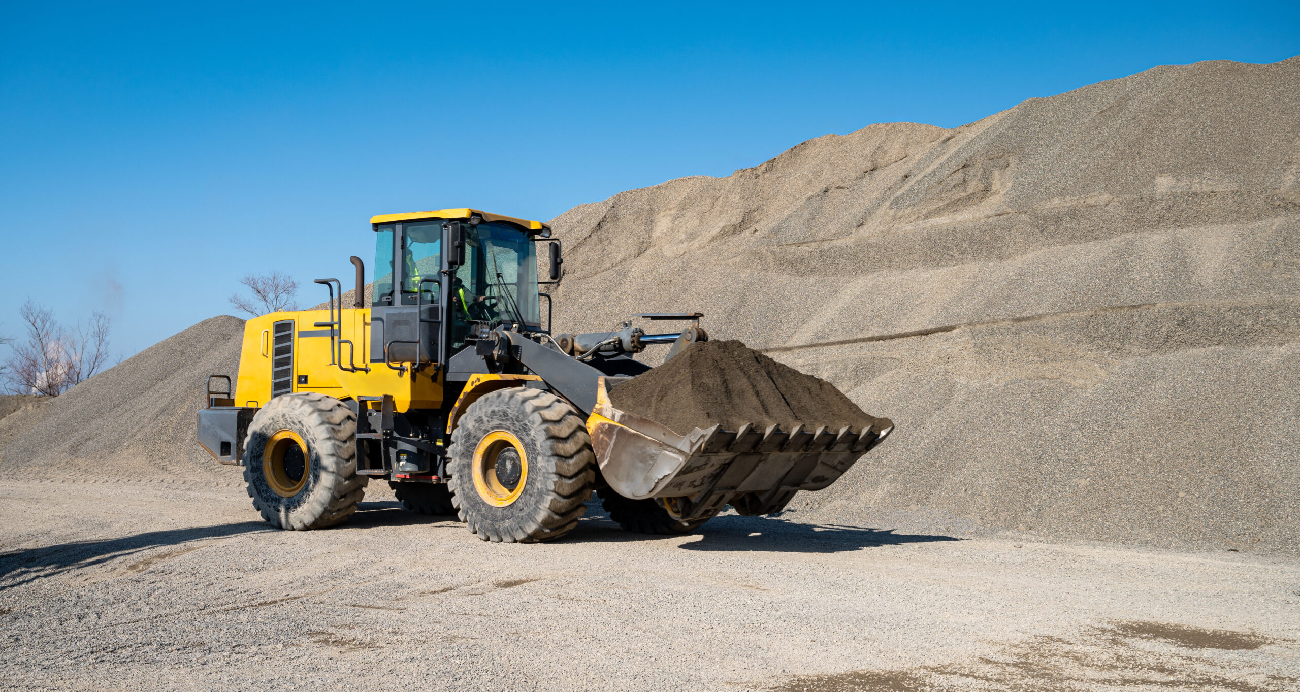 A large loader transports crushed rock or gravel in a bucket at a construction site or concrete plant. Concept of transporting bulk materials on construction equipment.